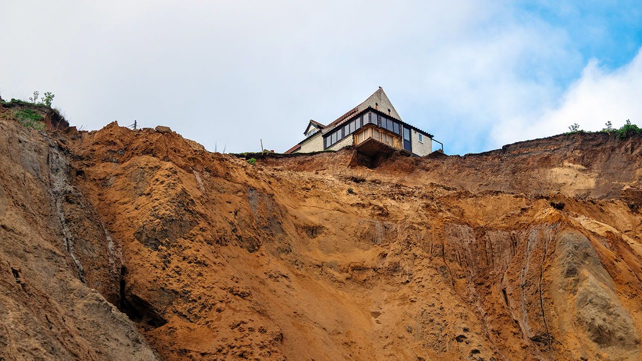 A house partially hangs over a cliff edge following rapid coastal erosion in Norfolk, United Kingdon