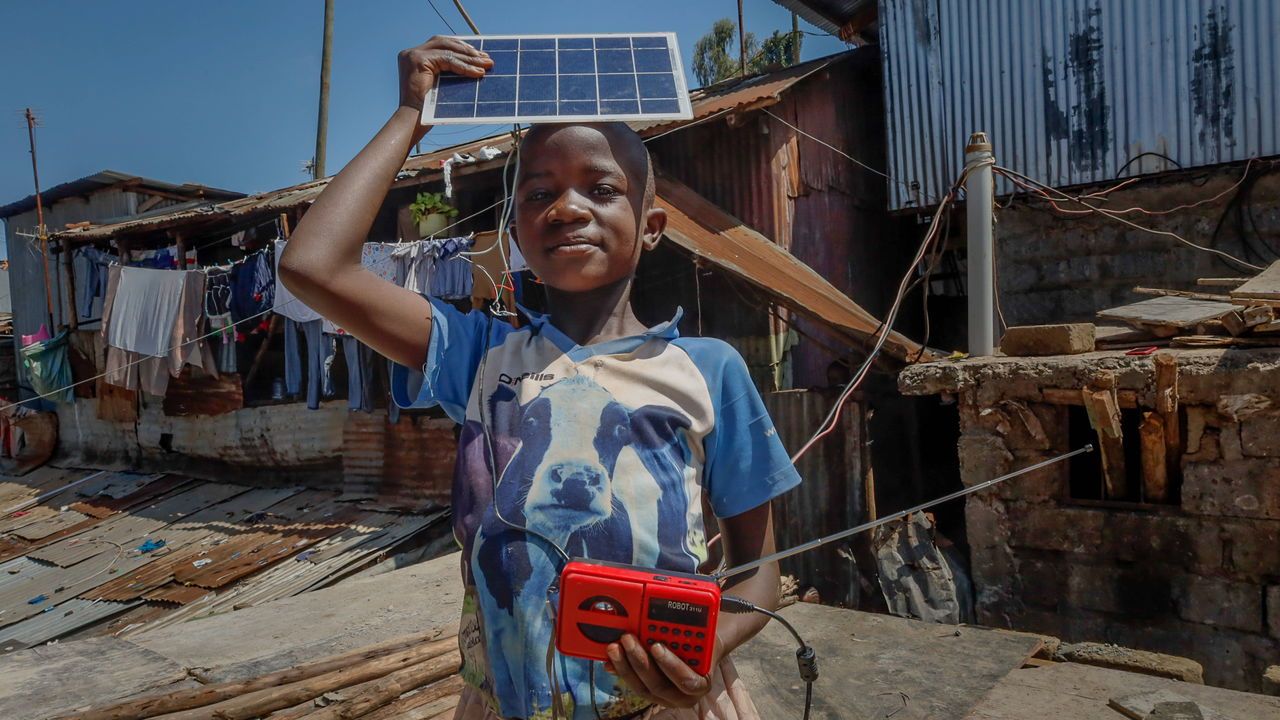 A young girl charges a radio using a modified solar panel in Kibera, Nairobi