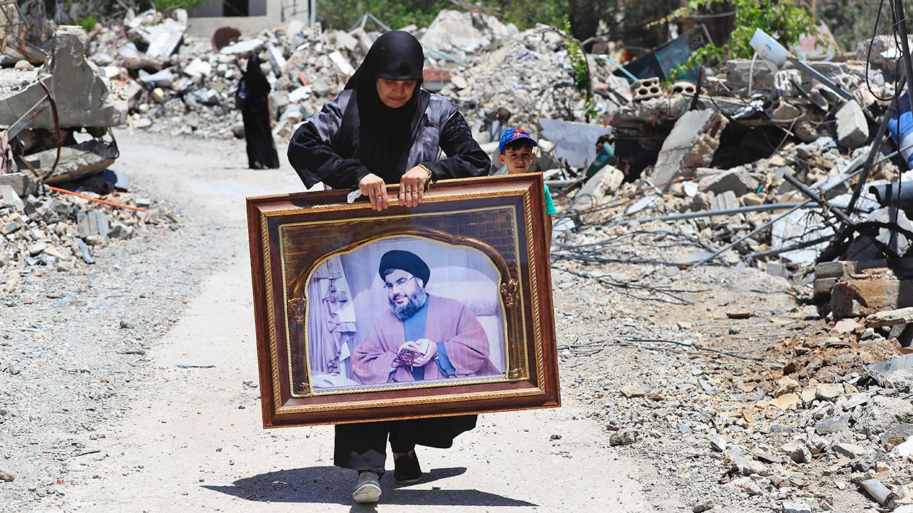 A woman carries a portrait of Hezbollah leader Sayyid Hassan Nasrallah past destroyed houses in Aita, Lebanon