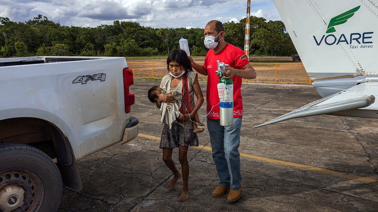 A Yanomami mother carrying her child who is sick with pneumonia and severe malnutrition disembarks from a small plane, assisted by a health workeR.