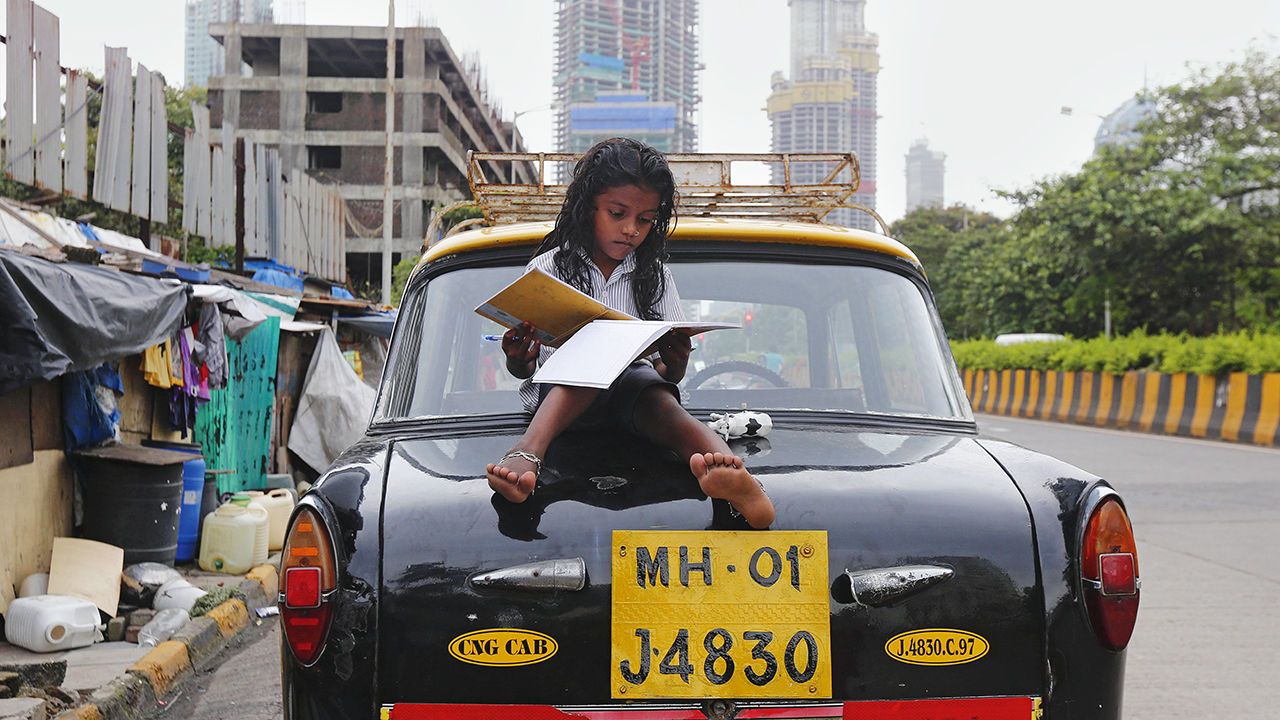 A girl studies while sitting on top of a taxi outside her shanty home at a roadside in Mumbai, India