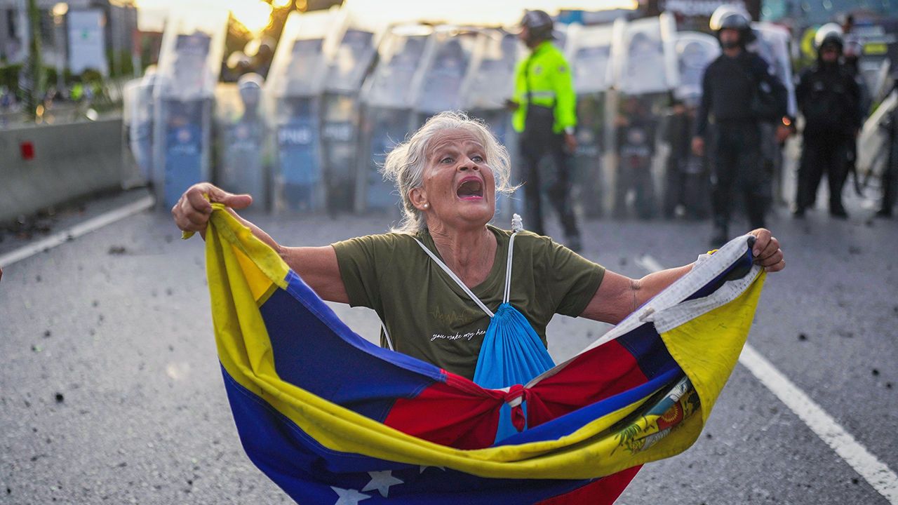 Consuelo Marquez holds a Venezuelan flag in front of police blocking demonstrations against the official election result in Caracas, Venezuela