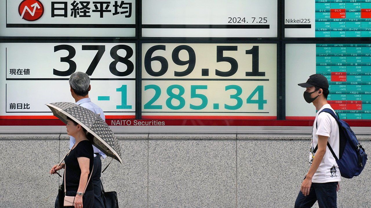 Pedestrians walk past a display showing the closing information of Tokyo's Nikkei Stock Average in Tokyo, Japan.